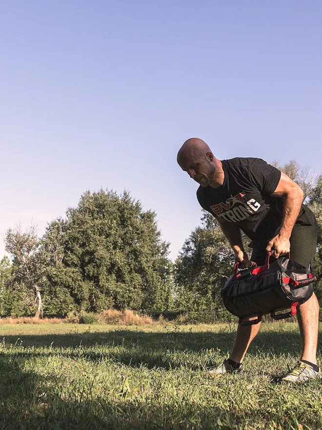 An adult lifting an Ultimate Sandbag outdoors on grass